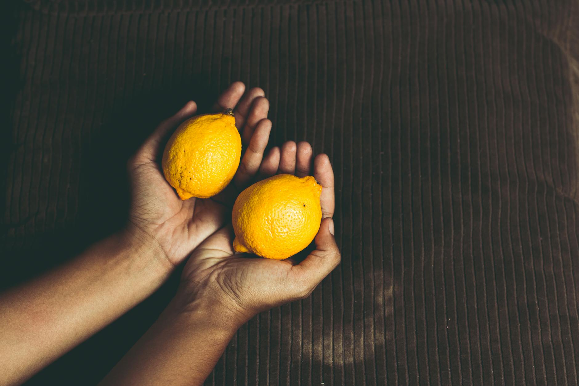 Deux citrons jaunes frais dans des mains en coupe sur une surface marron, symbolisant la fraîcheur et le plaisir naturel