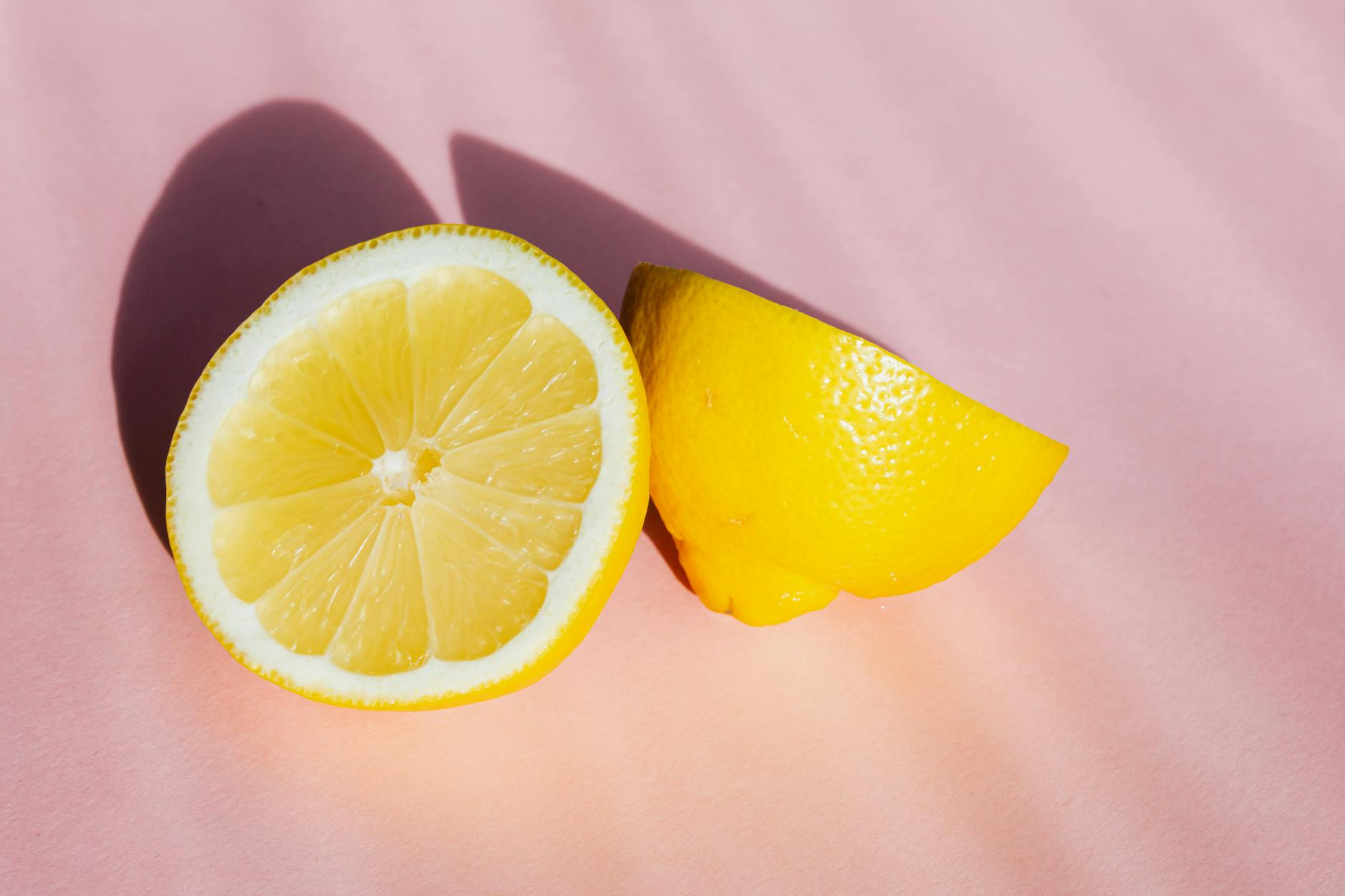 Une main tenant un citron frais sur un fond rose doux, entourée de trois autres citrons éclatants