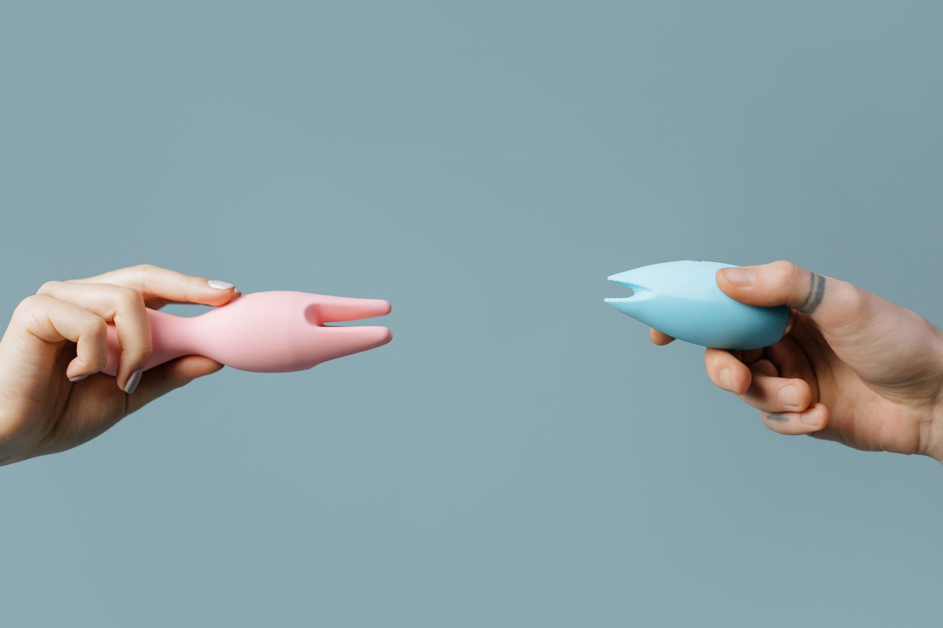 Deux mains tenant des vibromasseurs silicone rose et bleu sur un fond pastel