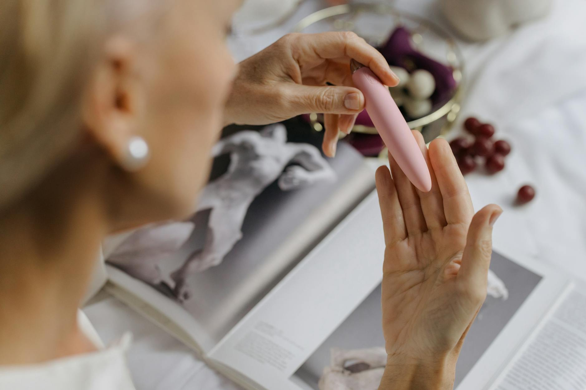 Close-up of a person holding a pink clitoral vibrator, with personal items in the background