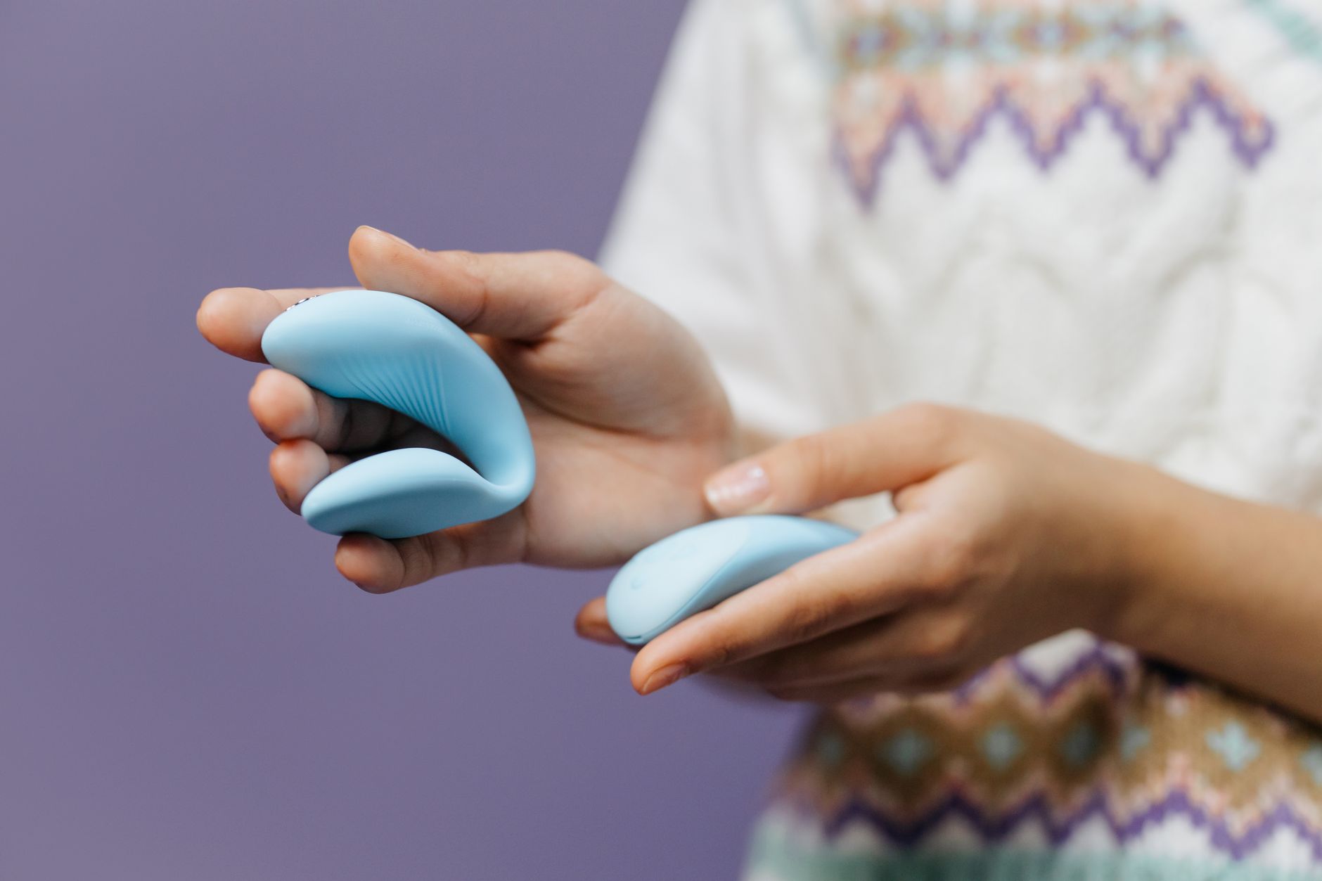 Mains tenant délicatement un vibromasseur bleu sur fond violet pastel