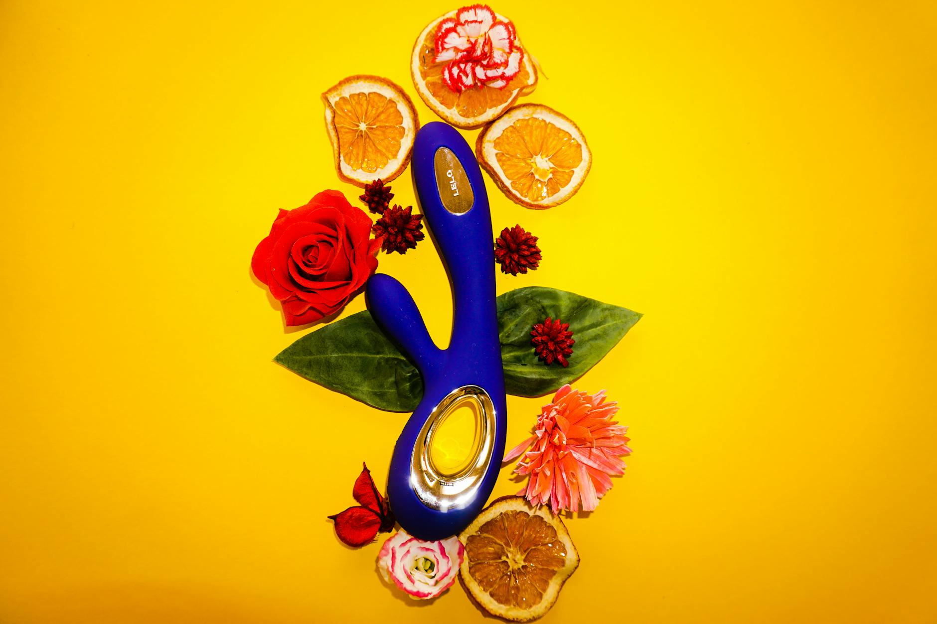 Un vibromasseur bleu entouré de fleurs et de tranches d'orange sur un fond jaune