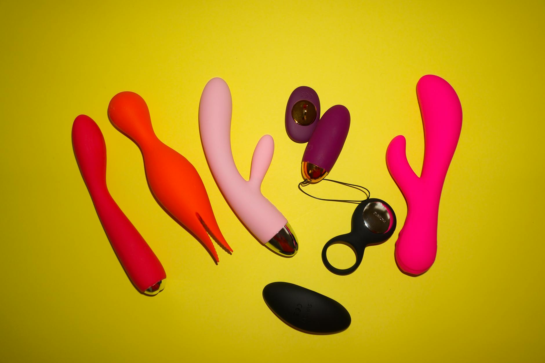 Collection de vibromasseurs colorés sur fond jaune vif dans un studio professionnel